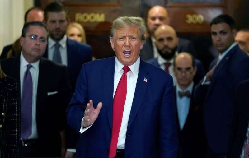 Man speaking gesturing with security behind him.