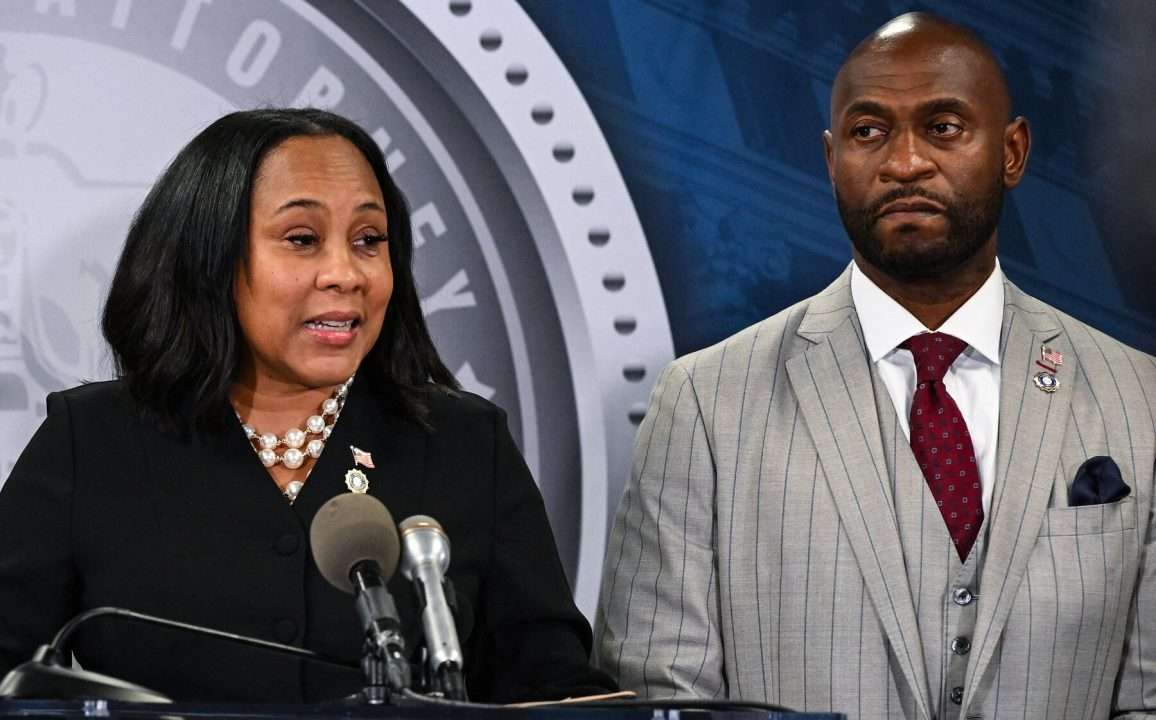 Woman speaking at podium, man listening behind.