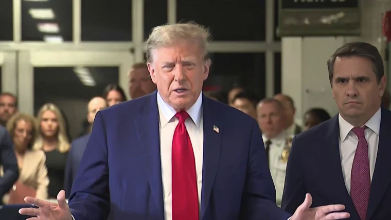 Man speaking at event with listeners in background.